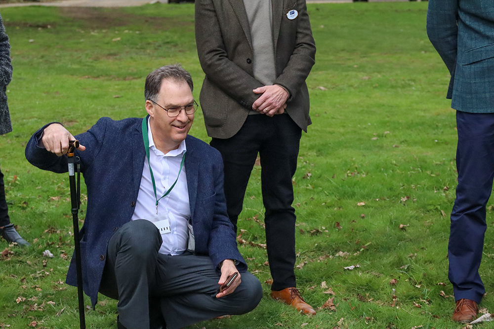 Andy Atkins kneeling and smiling while watching the planting of the Apricot tree