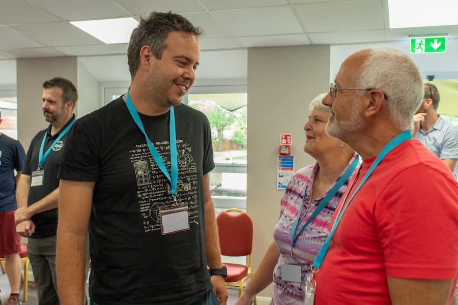 A man smiling and talking to an elderly couple in the Yew Tree Hall, enjoying being together.