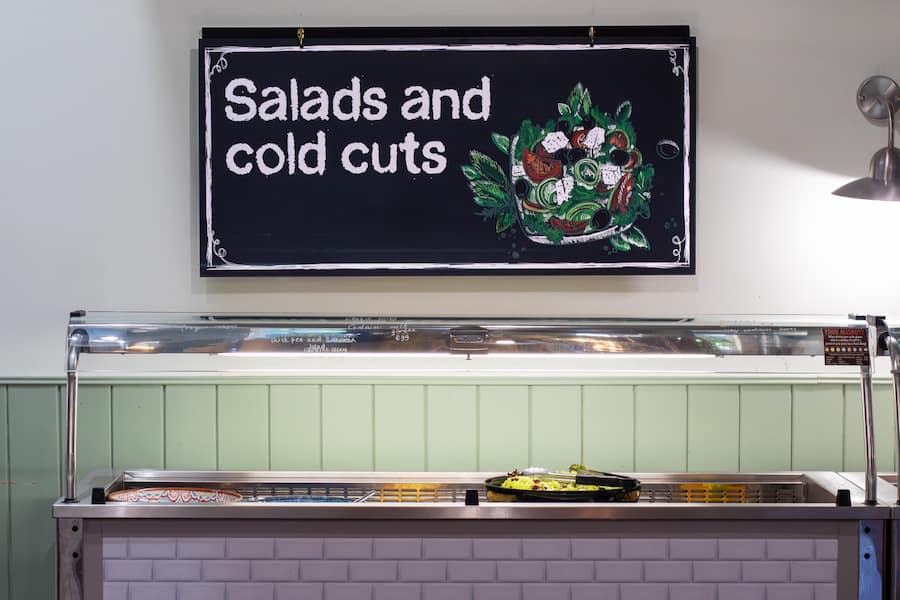 A large sign above the salads section which says, 'salads and cold cuts' with a colourful chalk drawing of a salad.