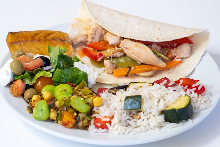 An image of a plate of high quality food with vibrant colours including 2 salads, a chicken fajita wrap, and rice.