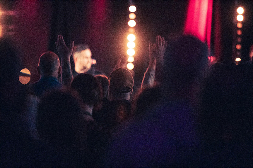 A man raising his hands in worship in a dark, ambient room