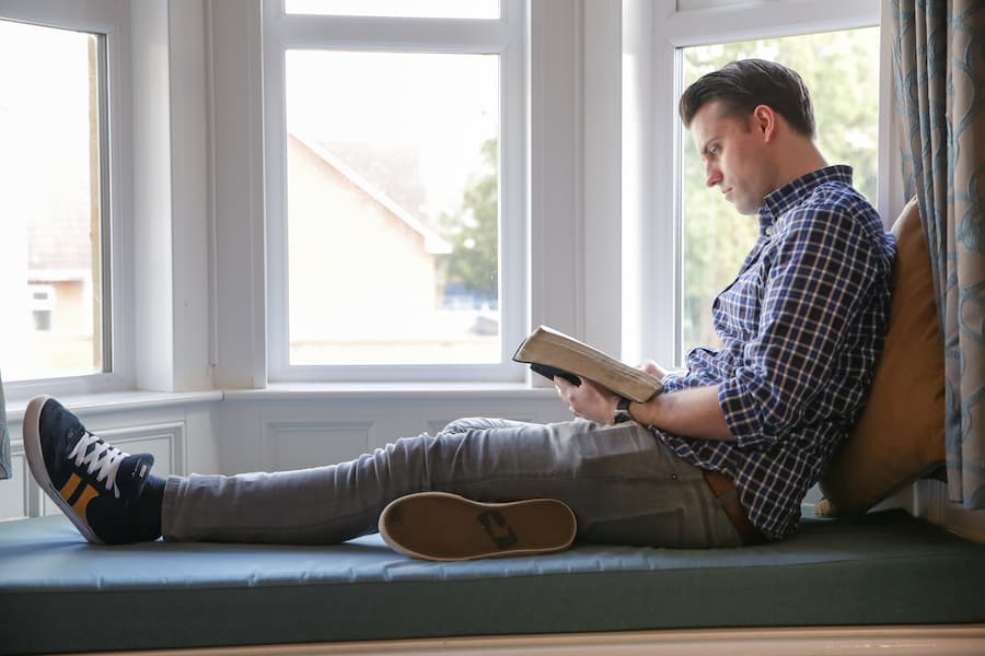 A man reading his Bible next to a window