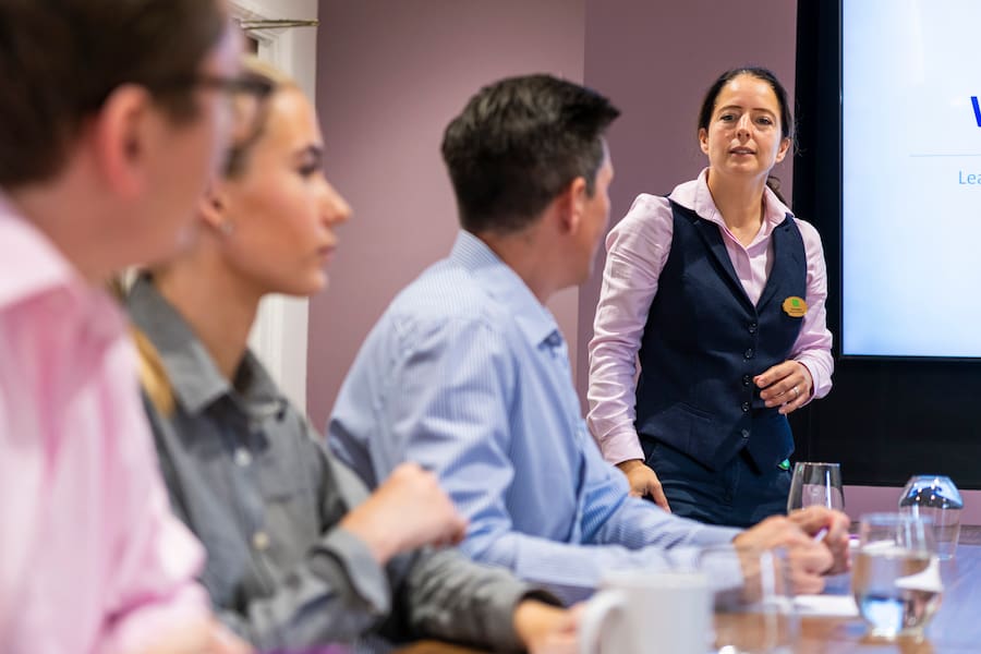 A woman talking up front in a boardroom set up about their action plan for the year.