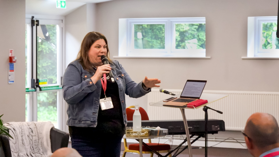 A woman in a denim jacket teaching in the Yew Tree Hall to students during the Christ for all nations Fire Camp