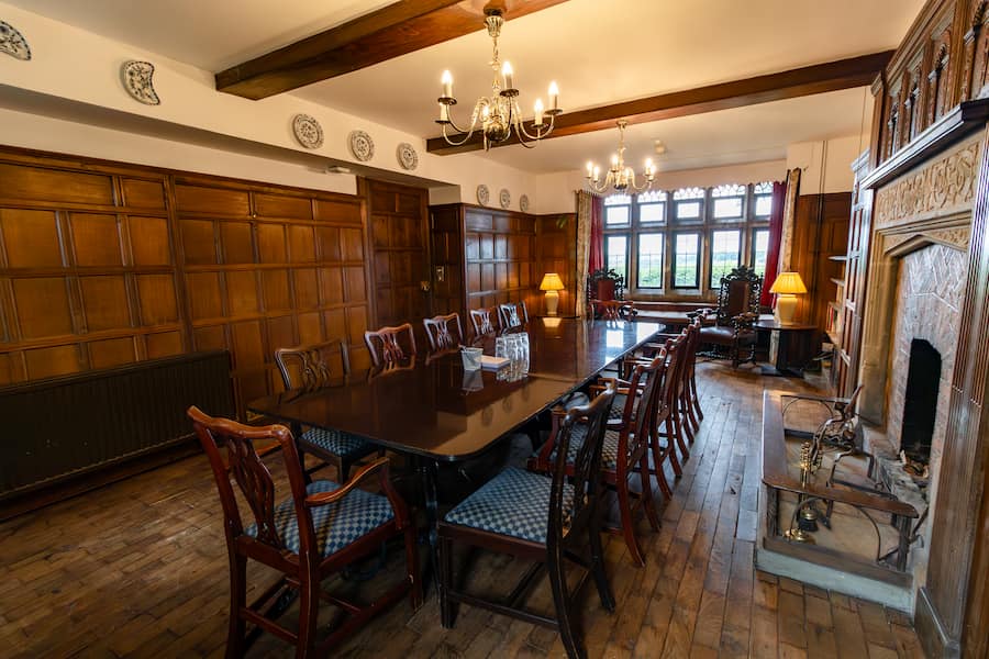 The Library meeting room showing the boardroom table and chairs, wooden panelling and floors and the fireplace to the right.