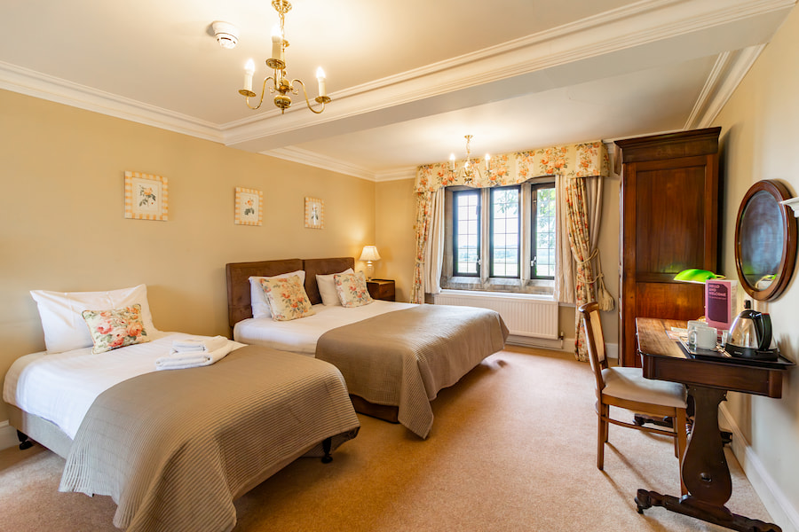 A family bedroom with a double bed and a single bed, a big wooden wardrobe, and a table and chair in front of a mirror.