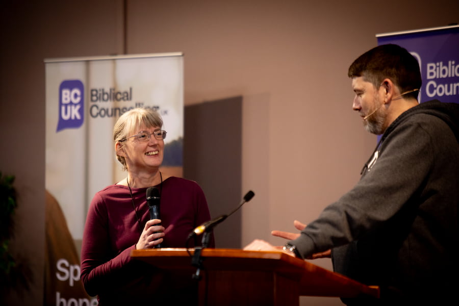 A woman talking to a man at a lectern on the stage in the Derbyshire hall during a session.