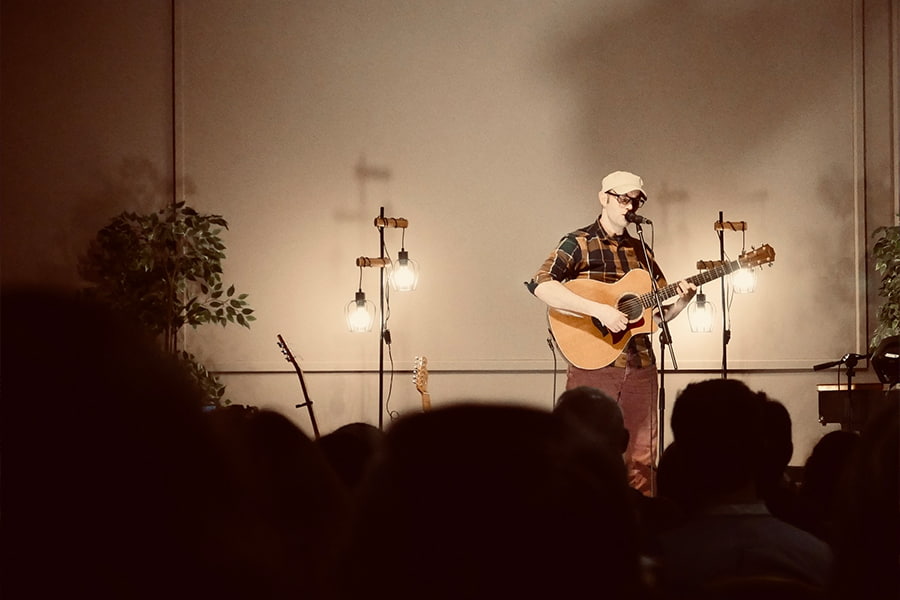 An image of a man on the stage of the Derbyshire Hall leading worship with a guitar with dim atmospheric lighting.