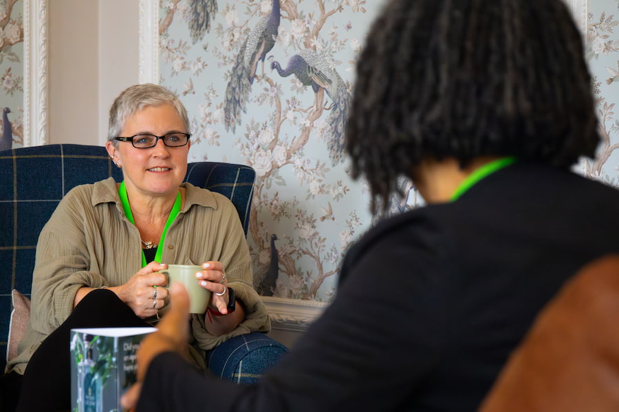 A woman sitting in a lounge at High Leigh Conference Centre with a cup of coffee listening to her friend.