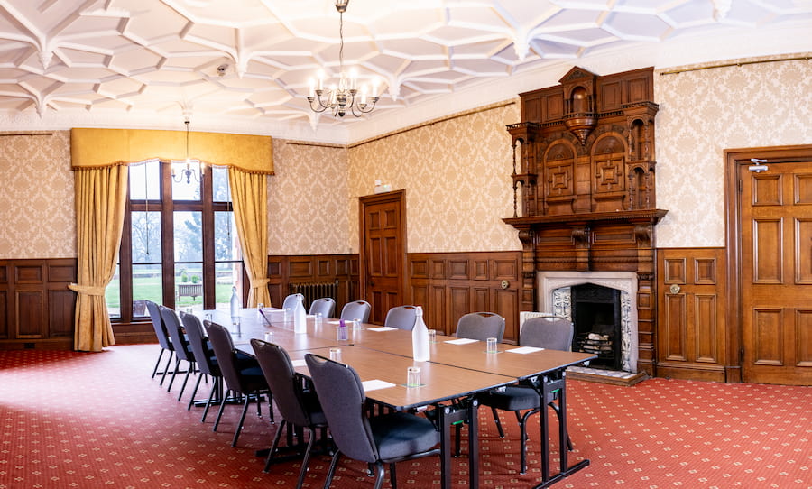 The Oak Room showing the boardroom table and chairs, the big windows, and the fire place with all the detailed woodwork. 