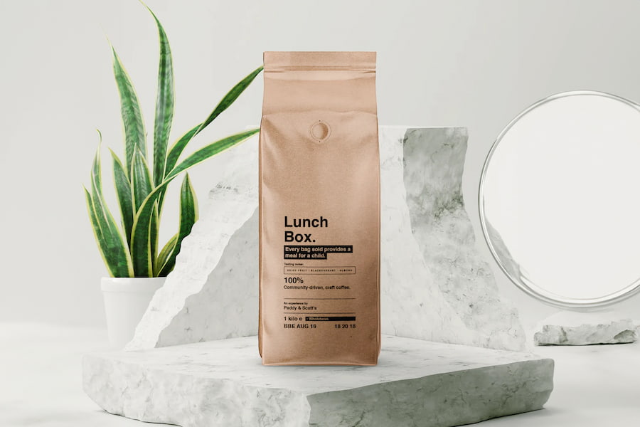 A bag of Lunch Box coffee beans sitting on a marble display stand with a plant in the background.