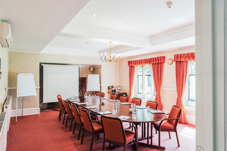 Pine room set out in boardroom style with red carpet, chairs and curtains and sun streaming through the windows.