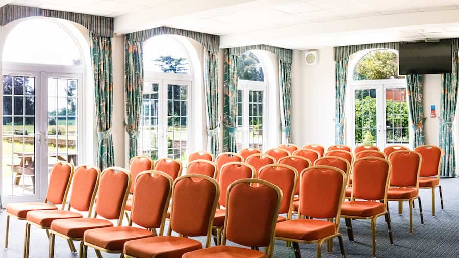 The Willow Hall with sun streaming through the floor-to-ceiling windows and orange chairs set out in theatre style.