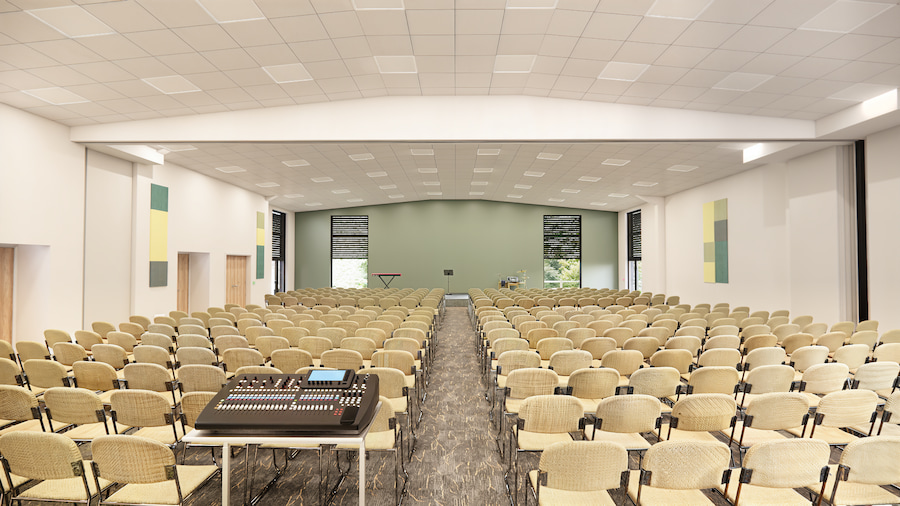 A 3d rendered image of the inside of the new meeting hall showing a huge hall with many chairs set out in theatre-style and a state-of-the-art mixing desk at the back.