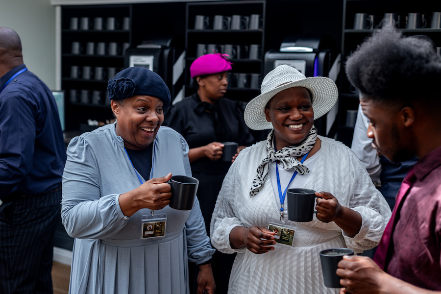 Two women in the coffee lounge each smiling while holding a cup of coffee.