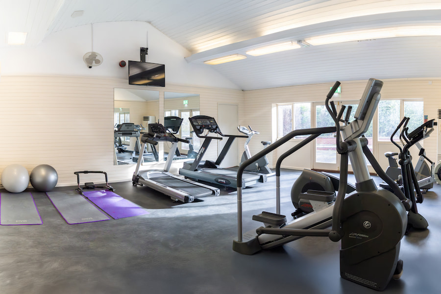 The gym with sun streaming through the windows showing 2 treadmills, a stationary bike, exercise mats and balls.