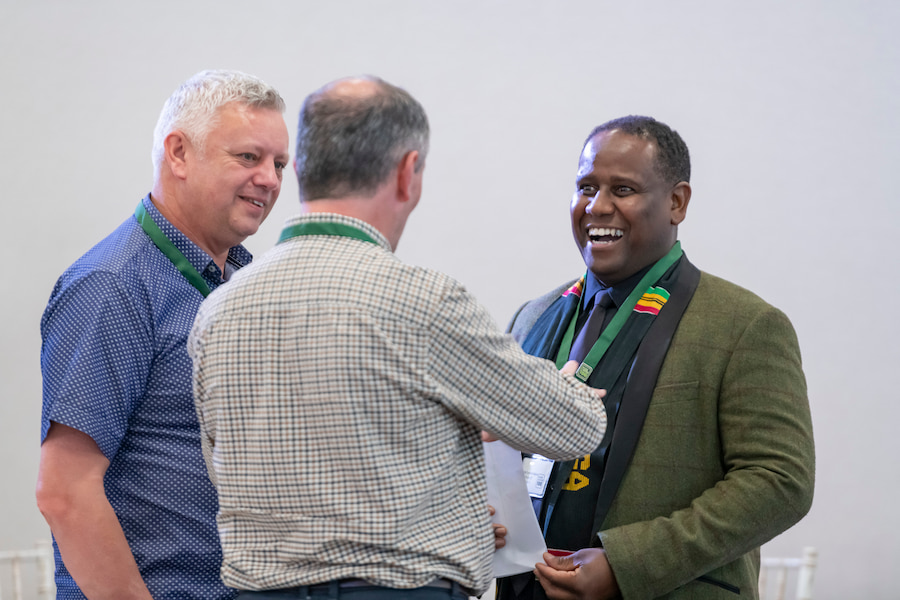 3 men talking to each other, 1 with his back turned and the other 2 smiling at him as if to find what he's saying funny.