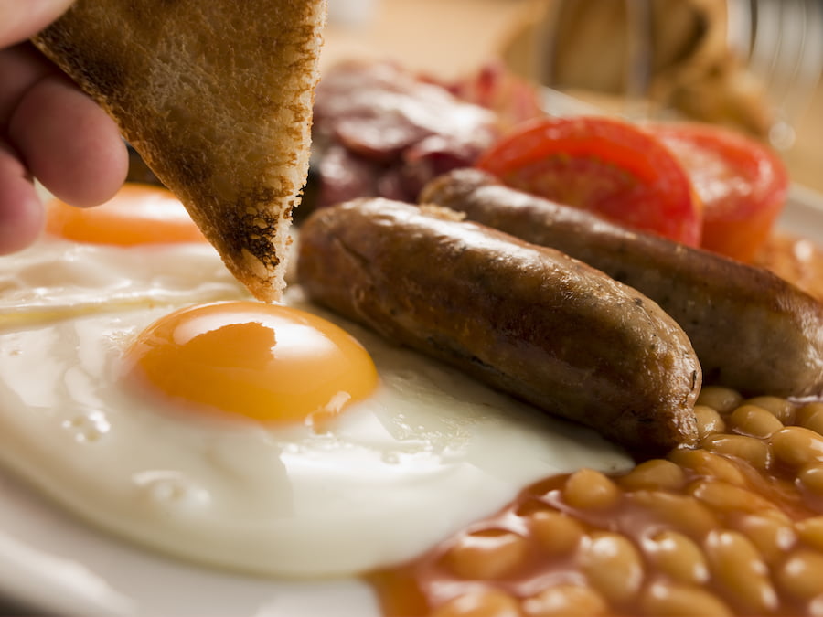 Dipping toast into a fried egg surrounded by beans, sausages and tomatoes.