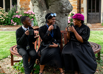 A young man and 2 women sitting outside Highgate House drinking coffee and talking.