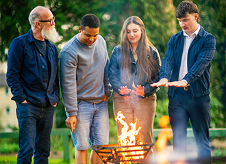 4 people standing around a bonfire talking and warming their hands.